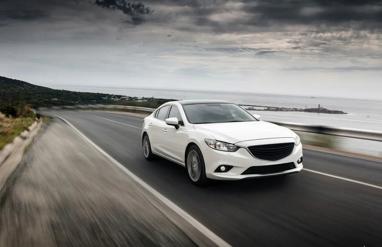 White sedan driving fast on coastal highway under cloudy sky, sleek design, ocean view